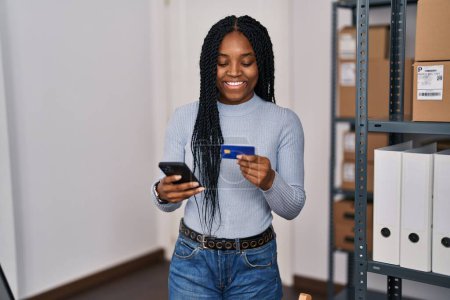 Téléchargez les photos : Femme afro-américaine e-commerce travailleur d'affaires en utilisant smartphone et carte de crédit au bureau - en image libre de droit