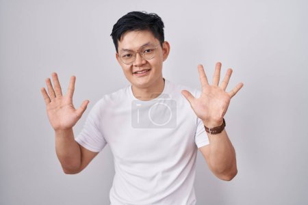 Téléchargez les photos : Jeune homme asiatique debout sur fond blanc montrant et pointant vers le haut avec les doigts numéro dix tout en souriant confiant et heureux. - en image libre de droit