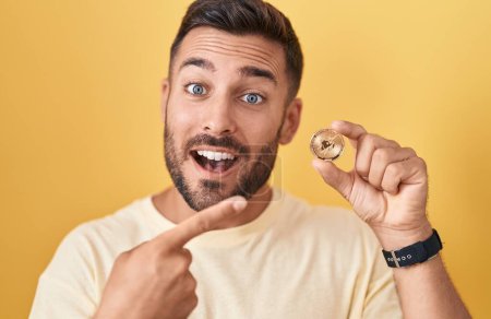 Téléchargez les photos : Bel homme hispanique tenant uniswap pièce crypto-monnaie sourire heureux pointant avec la main et le doigt - en image libre de droit