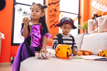 Foto de Adorable chico y chica teniendo fiesta de halloween sosteniendo caramelos en casa - Imagen libre de derechos