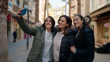 Photo for Mother and daugthers making selfie by the smartphone standing together at street - Royalty Free Image
