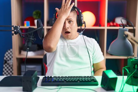 Téléchargez les photos : Young hispanic man playing video games surprised with hand on head for mistake, remember error. forgot, bad memory concept. - en image libre de droit