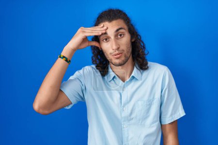 Photo for Young hispanic man standing over blue background worried and stressed about a problem with hand on forehead, nervous and anxious for crisis - Royalty Free Image