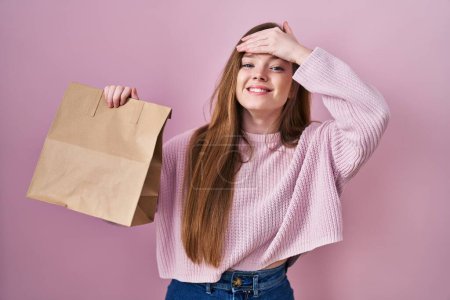 Foto de Mujer joven caucásica sosteniendo bolsa de compras y tarjeta de crédito estresada y frustrada con la mano en la cabeza, cara sorprendida y enojada - Imagen libre de derechos