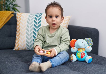 Foto de Adorable chico hispano jugando con juguete sentado en el sofá en casa - Imagen libre de derechos