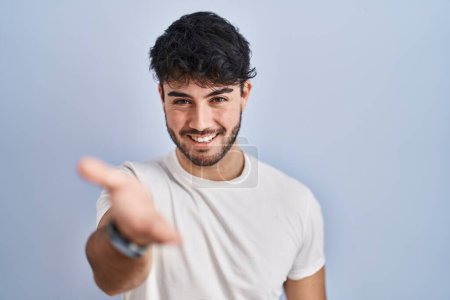 Téléchargez les photos : Hispanic man with beard standing over white background smiling cheerful offering palm hand giving assistance and acceptance. - en image libre de droit