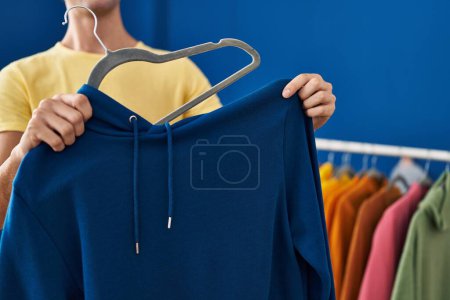 Photo for Young caucasian man putting sweatshirt on hanger at laundry room - Royalty Free Image