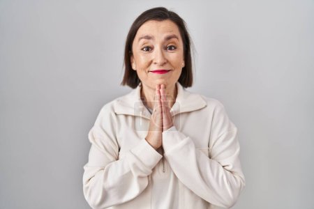 Photo for Middle age hispanic woman standing over isolated background praying with hands together asking for forgiveness smiling confident. - Royalty Free Image