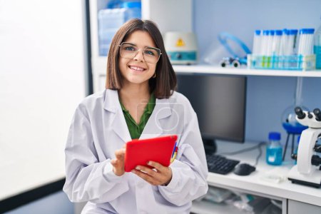 Photo for Young beautiful hispanic woman scientist smiling confident using touchpad at laboratory - Royalty Free Image