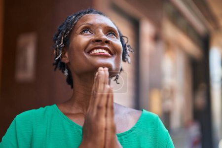 Téléchargez les photos : Moyen Age femme afro-américaine souriant confiant prier dans la rue - en image libre de droit