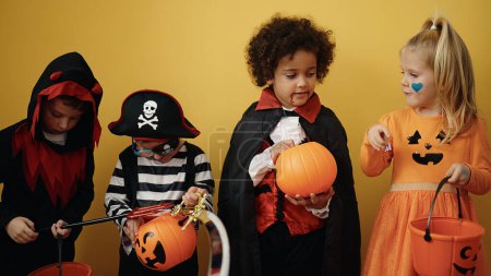 Téléchargez les photos : Groupe d'enfants portant un costume d'Halloween mettant des bonbons dans le panier de citrouille sur fond jaune isolé - en image libre de droit