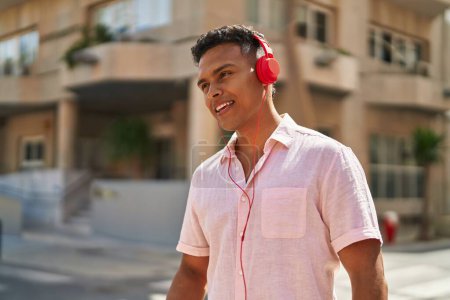 Téléchargez les photos : Jeune homme latino souriant confiant écoutant de la musique dans la rue - en image libre de droit