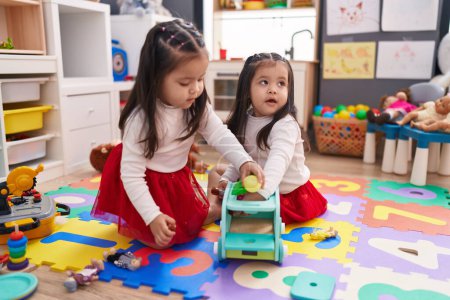 Foto de Adorable gemelas jugando con juguetes en el jardín de infantes - Imagen libre de derechos