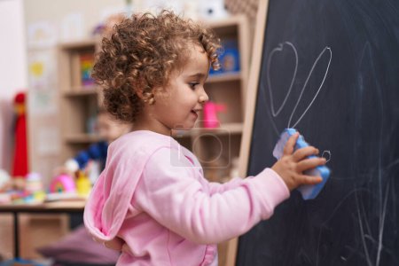 Photo for Adorable hispanic girl erasing blackboard at kindergarten - Royalty Free Image