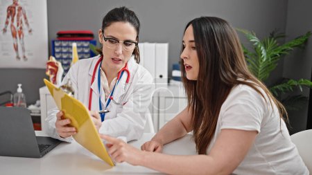 Photo for Two women doctor and patient prescribing pills writing on clipboard at clinic - Royalty Free Image