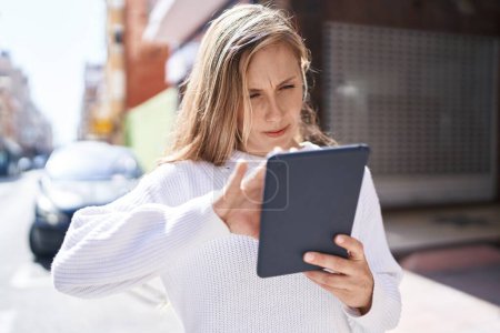 Téléchargez les photos : Jeune femme blonde utilisant touchpad avec une expression sérieuse à la rue - en image libre de droit