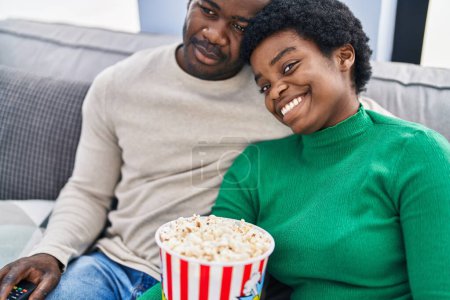 Foto de Africano americano hombre y mujer pareja viendo película comer palomitas de maíz en casa - Imagen libre de derechos