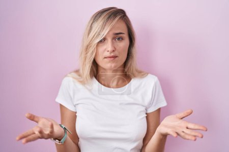 Photo for Young blonde woman standing over pink background clueless and confused with open arms, no idea concept. - Royalty Free Image