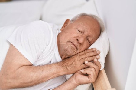 Téléchargez les photos : Homme âgé aux cheveux gris couché sur le lit dormant dans la chambre - en image libre de droit