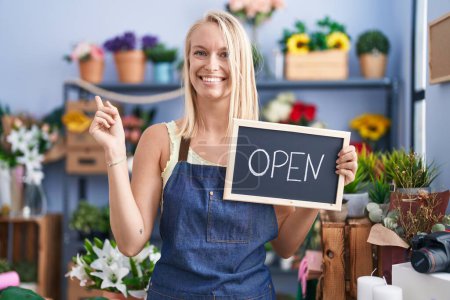 Photo for Young caucasian woman working at florist with open sign smiling happy pointing with hand and finger to the side - Royalty Free Image