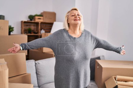 Photo for Middle age blonde woman breathing with arms open standing at new home - Royalty Free Image