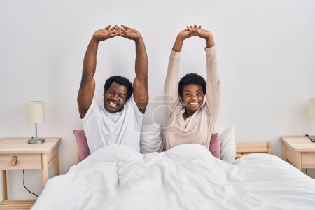 Photo for African american man and woman couple stretching arms sitting on bed at bedroom - Royalty Free Image