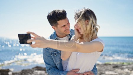 Photo for Man and woman couple standing together make selfie by smartphone at seaside - Royalty Free Image