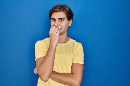 Photo for Young man standing over blue background looking stressed and nervous with hands on mouth biting nails. anxiety problem. - Royalty Free Image