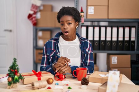 Photo for African american woman working at small business doing christmas decoration afraid and shocked with surprise expression, fear and excited face. - Royalty Free Image