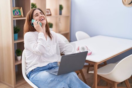 Photo for Young woman using laptop and talking on the smartphone at home - Royalty Free Image