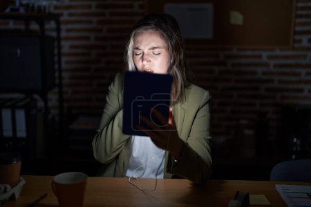 Photo for Blonde caucasian woman working at the office at night feeling unwell and coughing as symptom for cold or bronchitis. health care concept. - Royalty Free Image