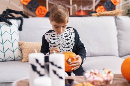 Photo for Adorable hispanic boy wearing skeleton costume drawing on pumpkin at home - Royalty Free Image