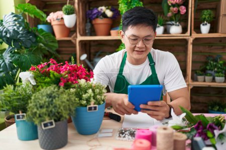 Téléchargez les photos : Jeune fleuriste chinois souriant confiant en utilisant le pavé tactile à la boutique de fleurs - en image libre de droit