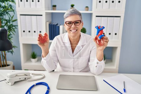Photo for Middle age woman wearing doctor uniform holding heart ventricles at clinic - Royalty Free Image
