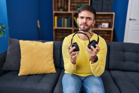 Photo for Hispanic man holding broken headphones skeptic and nervous, frowning upset because of problem. negative person. - Royalty Free Image