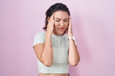 Foto de Mujer joven hispana de pie sobre fondo rosa con la mano en la cabeza, dolor de cabeza porque el estrés. padecer migraña. - Imagen libre de derechos