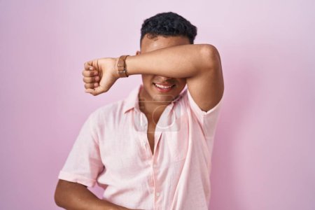 Photo for Young hispanic man standing over pink background covering eyes with arm smiling cheerful and funny. blind concept. - Royalty Free Image