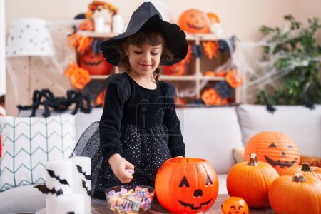 Foto de Adorable chica hispana teniendo fiesta de halloween sosteniendo dulce de tazón en casa - Imagen libre de derechos