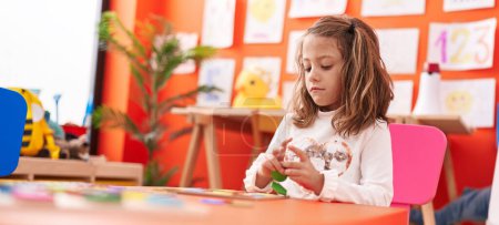 Téléchargez les photos : Adorable fille hispanique jouer avec des mathématiques jeu de puzzle assis sur la table à la maternelle - en image libre de droit
