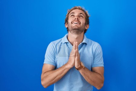 Photo for Caucasian man standing over blue background begging and praying with hands together with hope expression on face very emotional and worried. begging. - Royalty Free Image