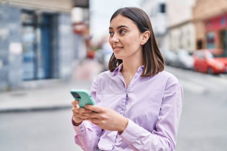 Téléchargez les photos : Jeune femme hispanique souriant confiant en utilisant smartphone à la rue - en image libre de droit