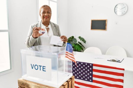 Foto de Mujer afroamericana mayor sosteniendo que voté la insignia votando en el colegio electoral - Imagen libre de derechos