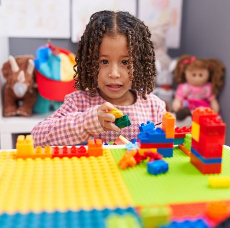 Téléchargez les photos : Africaine américaine fille jouer avec construction blocs assis sur la table à la maternelle - en image libre de droit