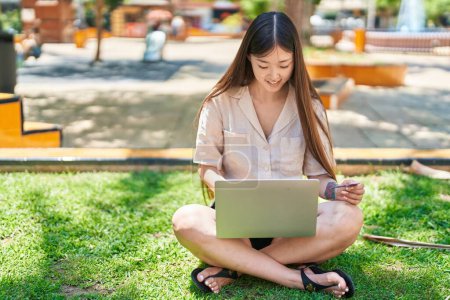 Foto de Chinese woman using laptop and credit card sitting on grass at park - Imagen libre de derechos