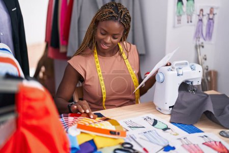 Téléchargez les photos : Femme afro-américaine tailleur tenant la conception de vêtements à la recherche test de couleur au magasin de tailleur - en image libre de droit