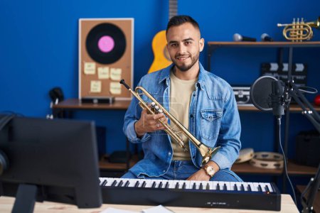 Foto de Joven músico hispano sonriendo confiado sosteniendo trompeta en el estudio de música - Imagen libre de derechos