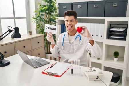 Photo for Young hispanic doctor man supporting organs donations sticking tongue out happy with funny expression. - Royalty Free Image