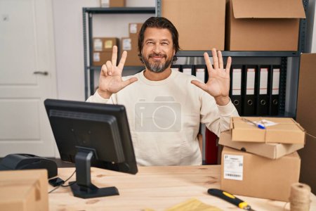 Foto de Hombre guapo de mediana edad que trabaja en el comercio electrónico de pequeñas empresas que muestra y señala con los dedos número ocho mientras sonríe confiado y feliz. - Imagen libre de derechos