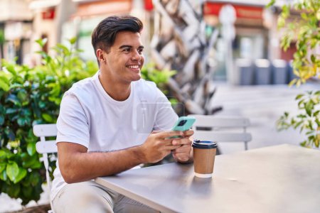 Téléchargez les photos : Jeune homme hispanique utilisant smartphone boire du café à la terrasse du café - en image libre de droit