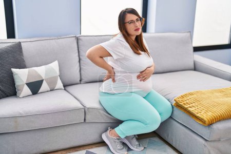 Foto de Mujer embarazada joven que sufre de dolor de espalda sentado en el sofá en casa - Imagen libre de derechos